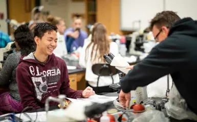 生物实验室的男学生对着显微镜微笑 
